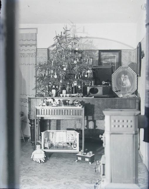 Gabentisch mit kleinem Weihnachtsbaum, Puppenstube, Grammophon und ansprechend gerahmter Fotografie (um 1925)