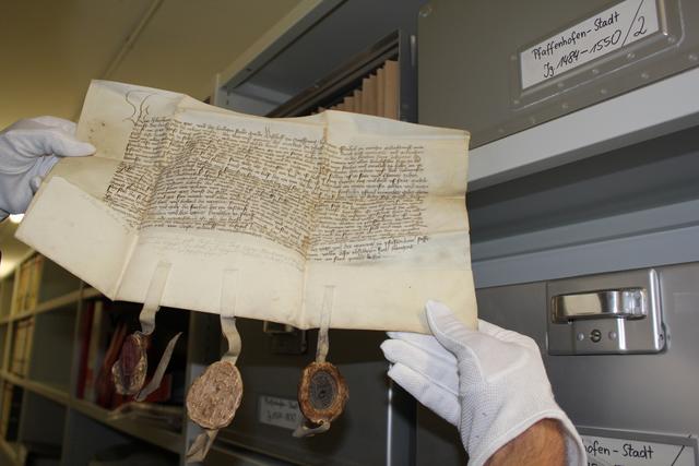 Konservatorisch richtige Handhabung und Unterbringung einer Stadturkunde aus dem Jahr 1409 mit Bischofs-, Abts- und Pfarrersiegel in Metallboxen.