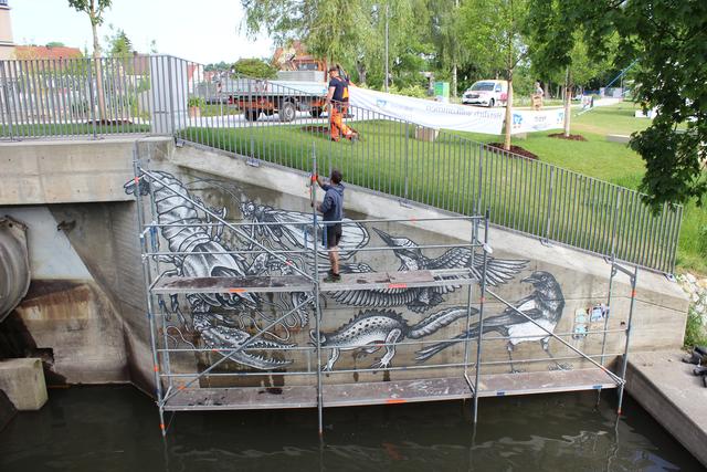 Das Rostrot am Wehr und das Grün am Ufer kommt gut zur Geltung, weil die Malerei farblos gehalten ist