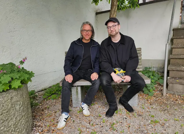 Zwei Männer auf einer Bank sitzend im Freien.