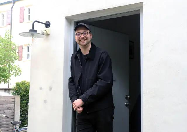 Mann lehnt an offener Haustüre und lächelt in die Kamera