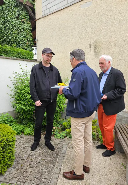 Drei Männer stehen im Freien, Geschenk wird überreicht
