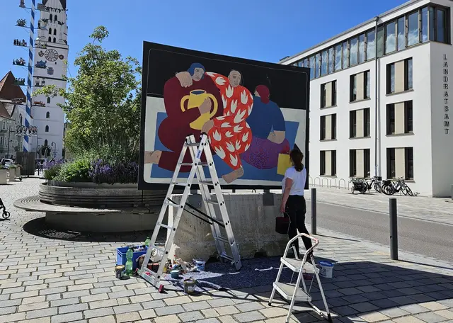 Künstlerin malt auf großer schwarzer Wand ein Kunstwerk auf dem Hauptplatz gegenüber des Landratsamts