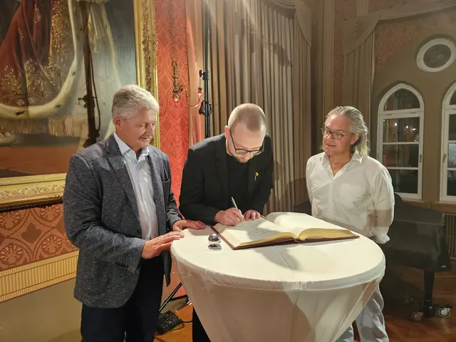 v.l.n.r. Zweiter Bürgermeister Peter Heinzlmair, Peter Thiers und Steffen Kopetzky an einem Stehtisch im Festsaal, Thiers unterschreibt in Goldenen Buch