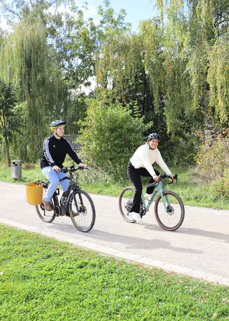 Ein Mann und eine Frau radeln durch einen Park. 