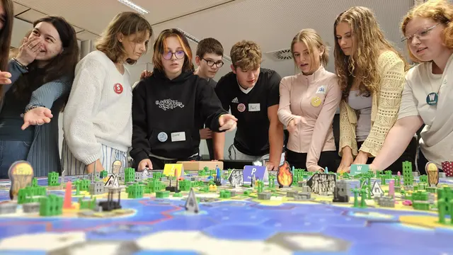 Schülerinnen und Schüler stehen rund um einen Spieletisch mit vielen Aktionsfiguren.