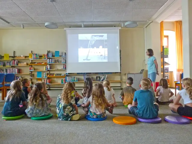 Kinder sitzen am Boden vor einer Leinwand in der Bücherei