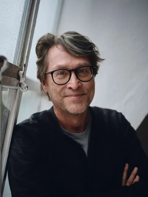 Portrait von Jan Weiler, er lehnt an einem Fenster und hat die Arme verschränkt