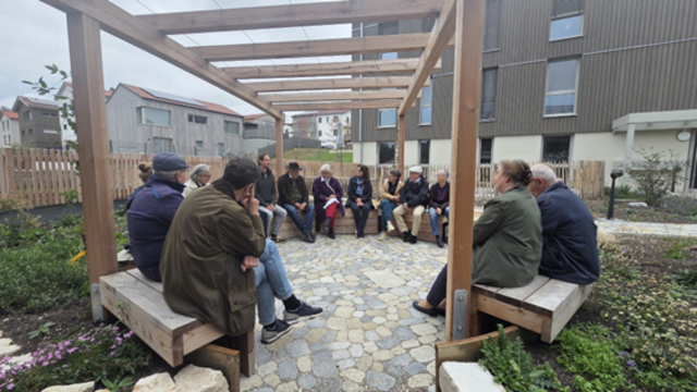 Erwachsene sitzen draußen im Garten der Wogeno im Kreis