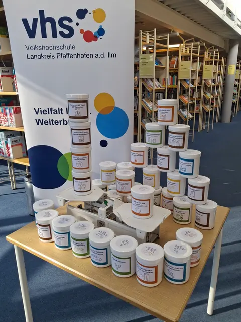 Auf einem Tisch steht eine Waage mit vielen beschrifteten Dosen
