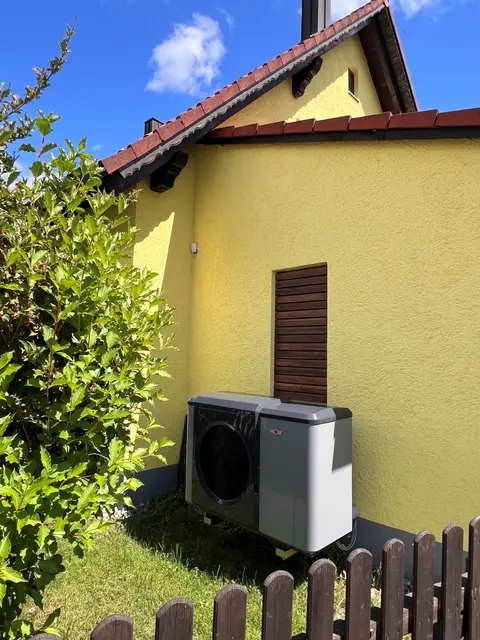 Wärmepumpe vor einem gelben Haus
